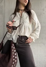 Camisa beige de manga larga, con detalles bordados en el frente y botones decorativos.
