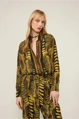 Camisa de viscosa estampada con diseño de plumas en tonos amarillo y negro. Tiene cuello clásico, mangas largas con puños abotonados, cierre frontal con botones y corte tradicional.
