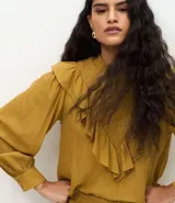 Blusa de manga larga color mostaza con cuello alto y detalle de panel delantero texturizado. Presenta volados aplicados en el busto y puños abotonados.
