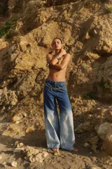 Jean de tiro medio con corte oversize y botamanga ancha. Presenta un diseño de lavado degradado que va de un azul intenso en la cintura a un tono claro en la parte inferior, con efecto gastado. Incluye avíos metálicos y badana de PU.