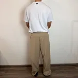 Pantalón sastrero color beige, de corte baggy, con pliegues en la cintura y bolsillos laterales.