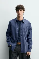 Camisa de corte regular fit en color azul, confeccionada en mezcla de lyocell y algodón, con cuello camisero, manga larga con puños abotonados, cierre frontal con botones y un bolsillo aplicado en el pecho.