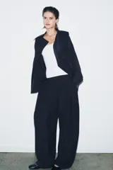 Pantalón de tiro medio con diseño wide leg, confeccionado en mezcla de lyocell. Presenta pinzas en el delantero y cierre frontal con cremallera, botón y ganchos metálicos.