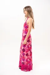 Vestido largo fucsia con estampado abstracto en tonos rosados y morados, cuello halter cruzado y flecos largos en el dobladillo inferior.