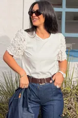 Remera blanca de algodón con mangas cortas abullonadas decoradas con apliques de flores en relieve. Presenta cuello redondo y un diseño versátil ideal para diversas ocasiones.