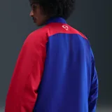 Campera deportiva Nike del Paris Saint-Germain, modelo Total 90 Reissue 2004, de color azul con una de las mangas en color rojo. Cuenta con cierre frontal completo, cuello alto y bolsillos laterales.