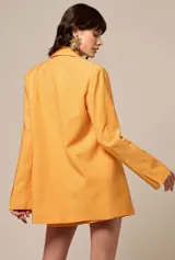 Blazer de corte sastre en color naranja, con solapas clásicas y manga larga. La prenda presenta un acabado texturizado con incrustaciones de strass en toda su superficie, aportando un brillo sutil y sofisticado.