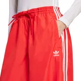 Pantalon Adidas de corte ancho y tiro alto, color rojo, con cintura elástica ajustable mediante cordón. Presenta las icónicas tres tiras blancas laterales y el logo del trébol bordado en la parte superior.