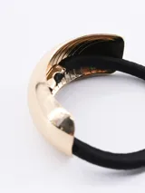 Colero elástico de color negro con un aplique metálico decorativo en tono dorado.
