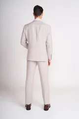 Traje de lino color beige claro, compuesto por saco de dos botones con solapa de muesca, dos bolsillos delanteros con solapa y un bolsillo en el pecho, y pantalón de vestir de corte recto. Incluye camisa blanca, corbata estampada y zapatos marrones.