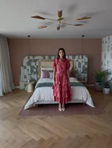 Vestido largo color rosado con volados en mangas y falda con capas. Tiene cuello camisero, mangas cortas abullonadas y cinturón de lazo en la cintura.