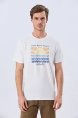 Remera blanca de manga corta y cuello redondo, con estampa frontal inspirada en el mar y atardeceres de verano con la inscripción 'Travel. Beach. Repeat.' y 'Legacy'.
