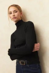Polera de tejido fino color negro, con cuello alto y mangas largas con terminación sutilmente fruncida. Diseño ajustado al cuerpo.