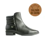Bota corta de cuero negro con textura granulada, diseño de caña acolchada en la parte superior y detalle de aplique metálico dorado en el lateral. Cuenta con taco bajo y suela de goma.
