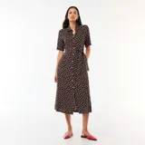 Vestido midi marrón con estampado de lunares blancos, estilo camisero con cuello solapa, mangas cortas, cierre frontal de botones y cinturón para anudar en la cintura.