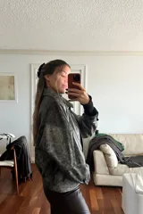 Campera bomber de cuero ovino con efecto desgastado en tonos grisáceos y negros. Presenta cuello camisero, cierre frontal con broches forrados y diseño holgado.