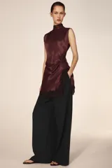 Vestido corto de cuello subido y sin mangas, confeccionado en tejido satinado. Presenta un detalle de fruncido lateral con abertura frontal y aplicación de encaje en el bajo.