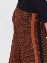 Pantalón de punto jacquard con diseño geométrico en tonos marrón y negro. Presenta un corte holgado de pierna ancha, tiro medio, cintura elastizada con cordón ajustable y una franja lateral lisa en color marrón.