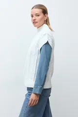 Chaleco de tejido de punto color crudo, con diseño de ochos verticales y cuello redondo. Presenta un corte holgado y terminaciones acanaladas en cuello, sisas y ruedo.