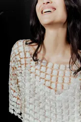 Blusa de red en color blanco con apliques de flores tridimensionales en toda la prenda. Presenta transparencias, cuello redondo y mangas largas.