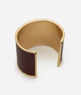 Pulsera rígida de metal con acabado en poliuretano color bordó y detalles dorados. Presenta una abertura para facilitar su colocación.