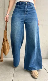 Jean wide leg de tiro medio-alto, color azul con lavado clásico y efecto desgastado. Presenta costuras laterales destacadas que estilizan la silueta, bolsillos delanteros y traseros, y cierre frontal con botón metálico y cremallera.