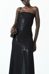 Vestido largo negro strapless con acabado brillante, corte ajustado en el torso y falda que cae recta con tajo frontal.