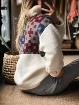 Buzo de corderito blanco con diseño de medio cierre frontal. Presenta un panel superior con estampado geométrico en tonos azul, gris y bordó, confeccionado con textiles vintage recuperados.