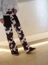 Pantalón vaquero de corte recto con estampado animal print tipo vaca en tonos marrón y blanco, con bolsillos delanteros de tela lisa y aberturas en los tobillos.