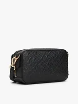 Cartera estilo camera bag negra, estructurada y compacta, con textura integral de monograma TH en relieve y placa metálica dorada con el logo TH en el frente. Posee cierre superior y correa ajustable para llevar al hombro o cruzada.