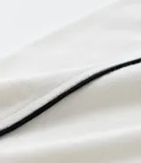 Remera tipo polo de hombre, color blanco crudo, con escote en V ribeteado en negro y ribetes negros en las costuras de los hombros. Presenta la inscripción arqueada "NEW YORK" en negro en el pecho.