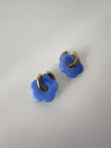 Aros de acero quirúrgico dorados con argollas pequeñas y dijes colgantes en forma de flor color celeste.