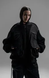 Campera estilo bomber unisex, confeccionada en una combinación de corderito sintético y paneles de ripstop. Presenta un diseño utilitario con múltiples bolsillos frontales con cierres y broches a presión, cuello, puños y ruedo en ribb elástico.