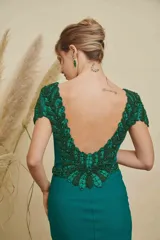 Vestido largo de fiesta color verde esmeralda, con escote ilusión, mangas cortas con detalles de pedrería y bordados, y cintura marcada con aplique de pedrería. Presenta una falda con caída fluida y pequeña cola.