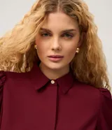 Camisa de crepé color blanco, con cuello inglés, manga larga abullonada con puños abotonados y cierre frontal oculto con botón diferenciado en el cuello.