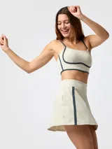 Set deportivo color beige con detalles en azul marino, compuesto por un top de tirantes finos y una pollera pantalón con diseño evasé y franja lateral contrastante.