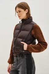 Chaleco acolchado de corte corto, color verde oliva, con cuello alto ajustable mediante cordones elásticos y cierre frontal con cremallera.