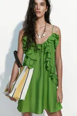 Vestido evasé corto de color verde, confeccionado en mezcla de viscosa con leve brillo. Presenta breteles finos ajustables, escote en U con cordón de ajuste y volados decorativos fruncidos en la parte superior.