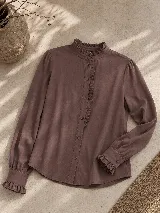 Camisa de manga larga color blanco, con cuello alto y detalle de volados en el cuello y a lo largo de la botonadura frontal. Presenta puños con volados y cierre de botones.