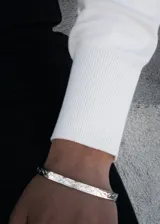 Pulsera esclava abierta de acero quirúrgico plateado con diseño esculpido en los extremos.