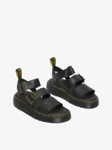 Sandalia Dr. Martens Gryphon Quad negra con plataforma, fabricada con piel Pisa. Presenta tres correas ajustables con hebillas de latón, pespuntes amarillos distintivos en la suela y tirador trasero con el logo AirWair.