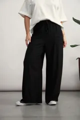 Pantalón de corte amplio y tiro alto, color negro, con cintura elástica y cordón ajustable. Presenta bolsillos laterales y costuras verticales decorativas en el frente.