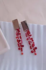 Caravanas colgantes con base rectangular de alpaca y múltiples tiras de cuentas de cristal facetadas en tonos rojos.