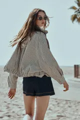 Chaqueta estilo bomber con estampado de cuadros vichy en blanco y negro, de cuello subido, manga larga y bolsillos delanteros de vivo. Cuenta con bajo abullonado y cierre frontal con cremallera oculta.