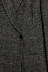 Blazer oversize de Zara confeccionado en hilatura con lana, con diseño de cuadros en tonos grises y líneas finas rojizas. Presenta cuello con solapa de muesca, cierre frontal cruzado con un botón, bolsillos de vivo en el delantero y forro interior.