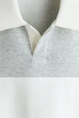 Buzo gris melange con cuello polo y solapa blanca, manga larga, hombros caídos y una franja horizontal blanca en el pecho.