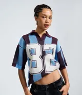 Remera de punto con diseño sportcore, cuello polo y mangas cortas amplias. Presenta un patrón de rayas verticales en tonos azul y bordó, con el número 82 estampado en el frente.