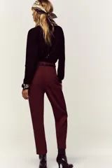 Pantalón de tiro alto y corte tobillero, confeccionado en tejido de aspecto denim oscuro. Presenta diseño de pinzas frontales, bolsillos laterales y cierre frontal con cremallera, botón y gancho. Incluye un cinturón fino a tono con hebilla metálica dorada.
