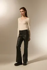 Pantalon de eco-cuero negro, de corte flare con costuras verticales frontales y detalle de tajo en el ruedo.