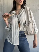 Camisa a rayas verticales color crudo y gris, de corte holgado y mangas largas con puños abotonados.